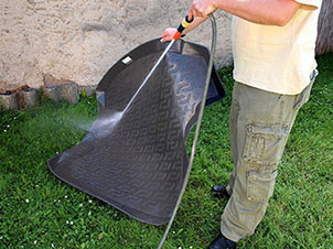 Kofferraumwanne-reinigen1 Ein Mann spritz mit Wasser eine Wanne ab.